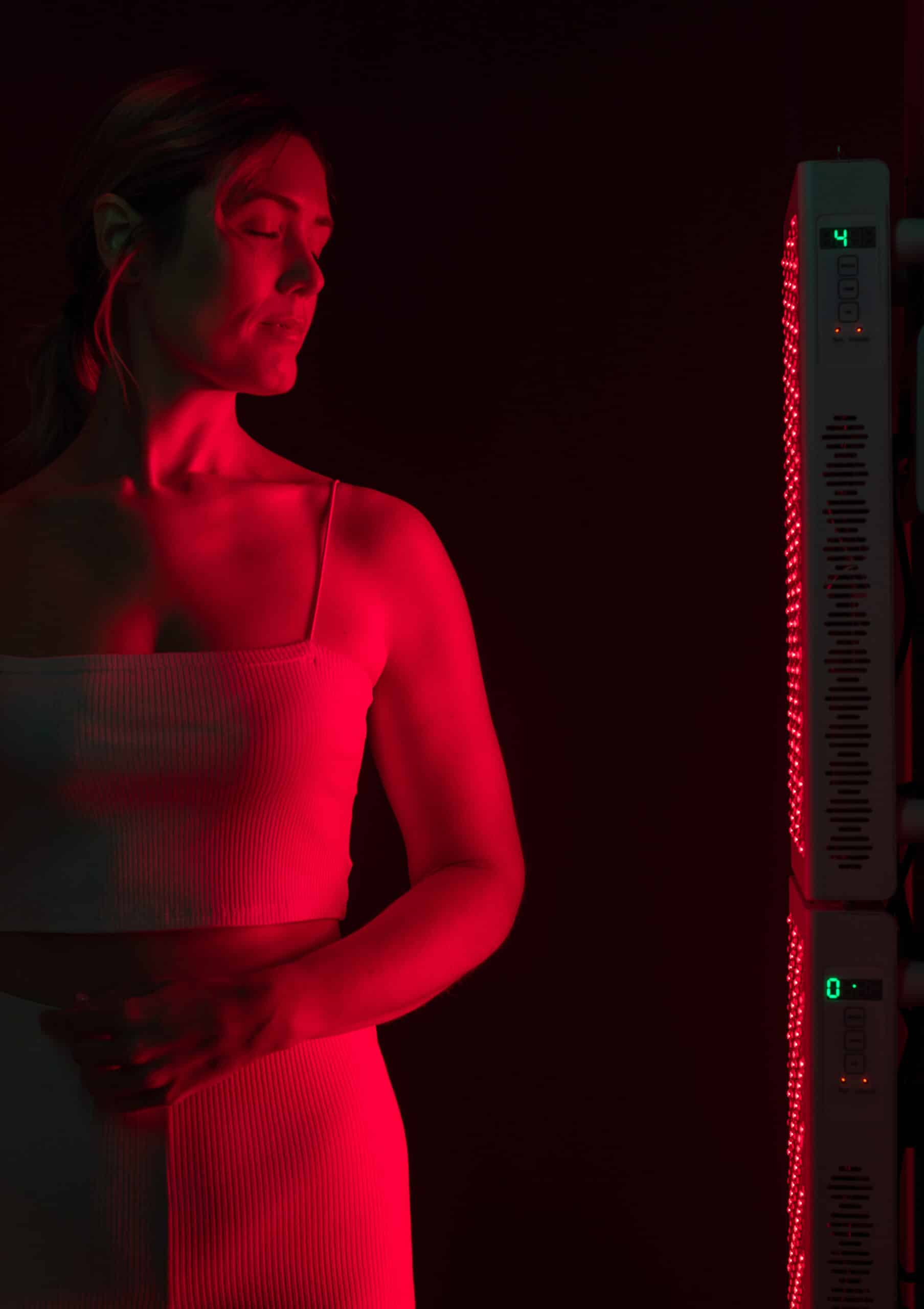 Woman getting red light therapy in a beauty spa. Mature woman standing next to a red light device. Anti-aging and skin care treatment.